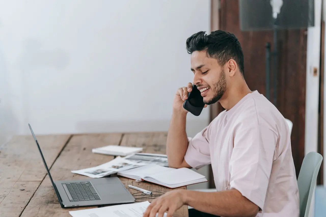 A smiling man on a phone call at his laptop