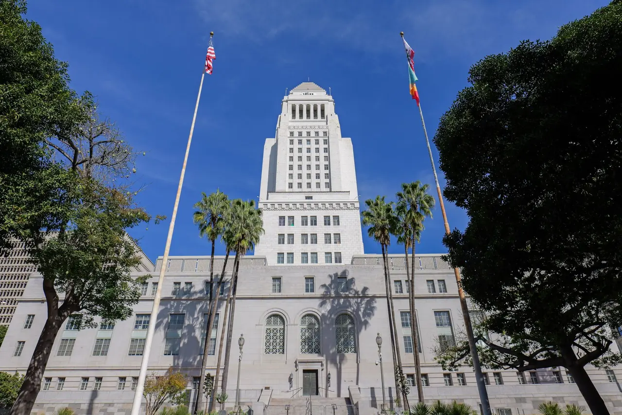 Los Angeles City Hall framed by palm trees and flags under a clear blue sky