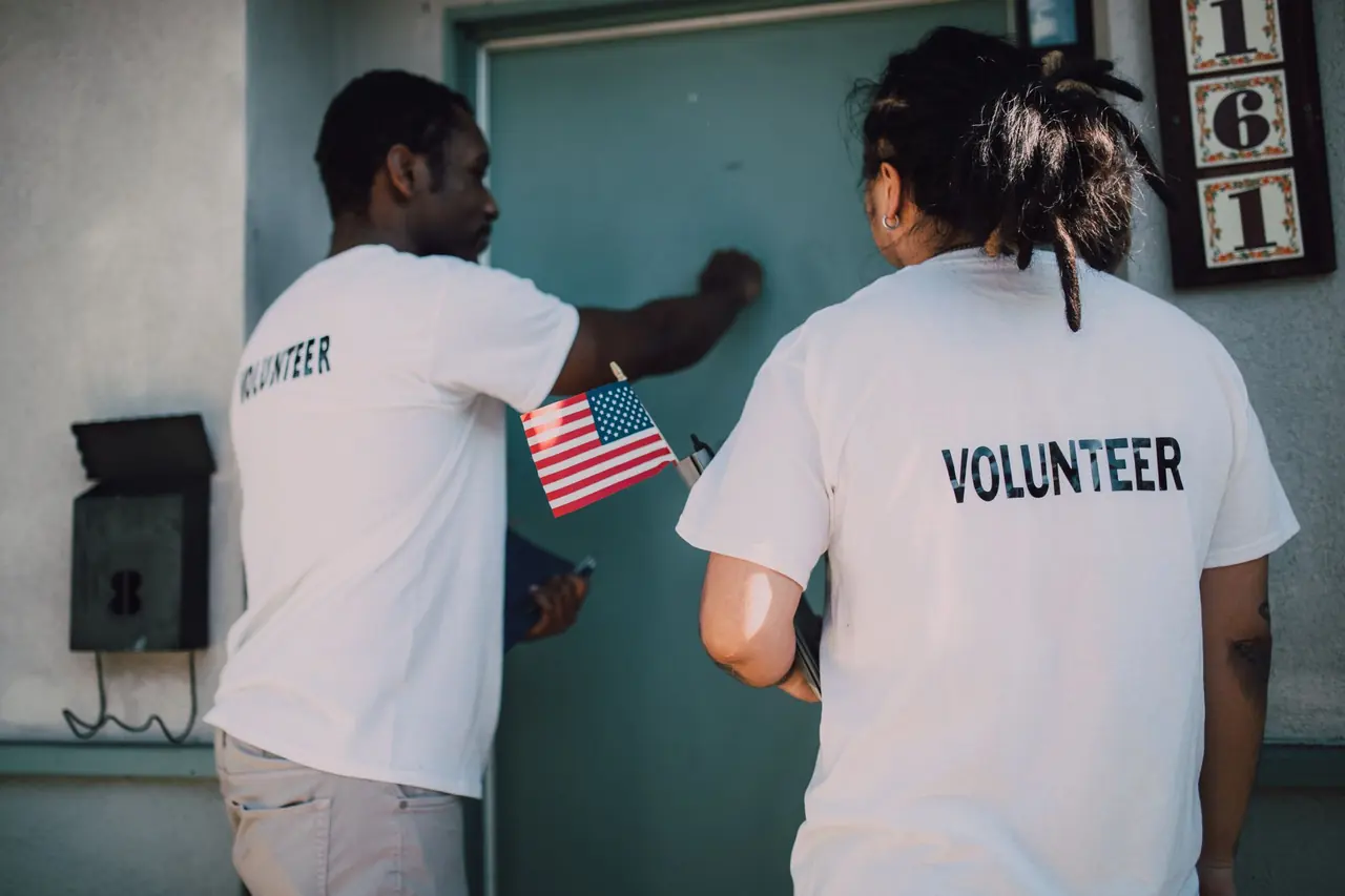 Two volunteers knocking on a front door while canvassing a neighborhood